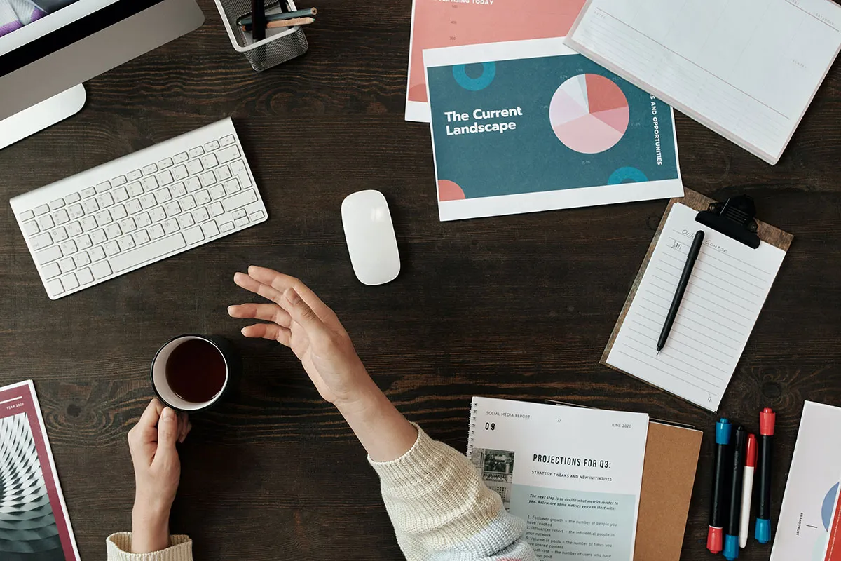 Overview shot of person with drinking coffee with documents and computer peripherals.