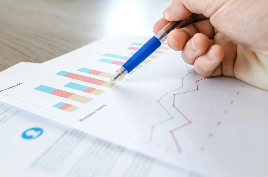 Person reviewing printed documents depicting charts & graphs, pointing a pen at a particular spot on a graph.