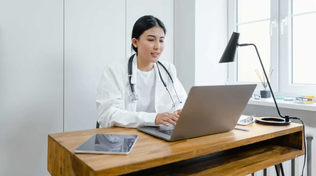 Female doctor with stethoscope around her neck at a computer performing telemedicine meeting.