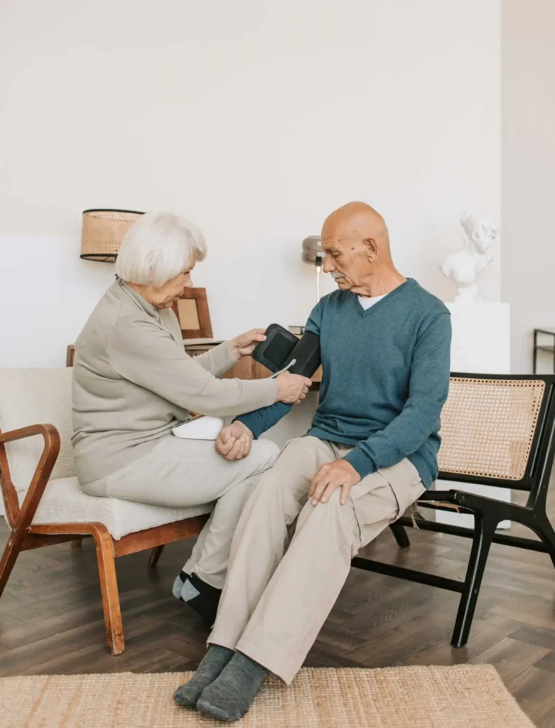 Older woman sitting down taking the blood pressure of an older man.